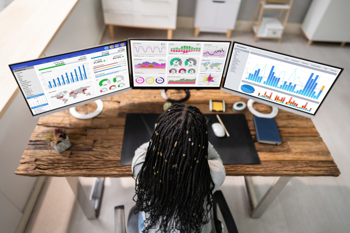 Understanding Google's Core Web Vitals and Its Impact on SEO 4 Person with braided hair working at a desk with three monitors displaying charts, graphs, data analytics, and core web vitals in a modern office setting.