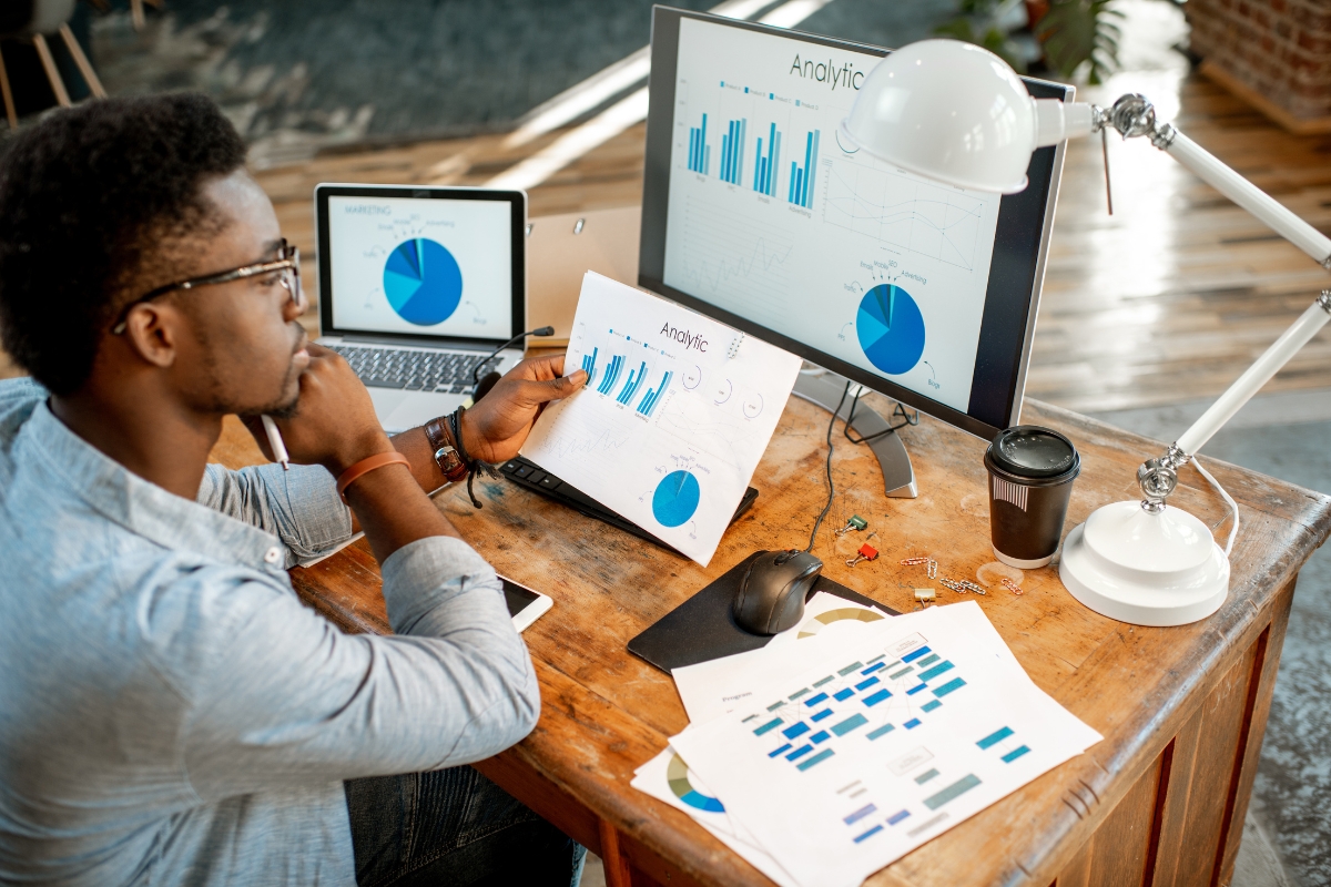 Understanding Google's Core Web Vitals and Its Impact on SEO 5 A person sits at a desk analyzing printed graphs, with core web vitals analytics displayed on a computer monitor and laptop; various charts and office items are visible on the wooden desk.