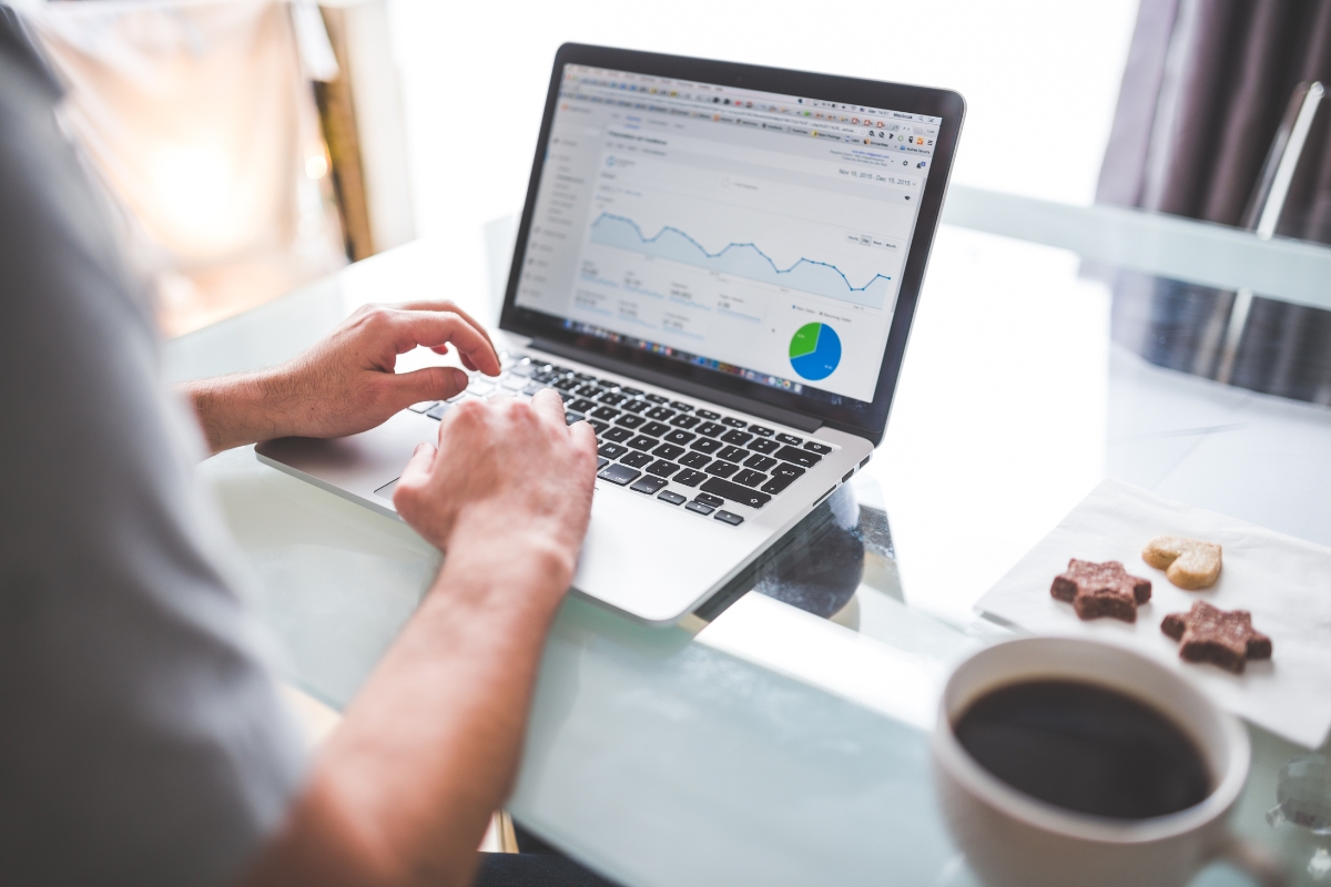 Understanding Google's Core Web Vitals and Its Impact on SEO 7 Person uses a laptop displaying an analytics dashboard with graphs, a pie chart, and core web vitals metrics, next to a cup of coffee and a plate of cookies on a glass table.