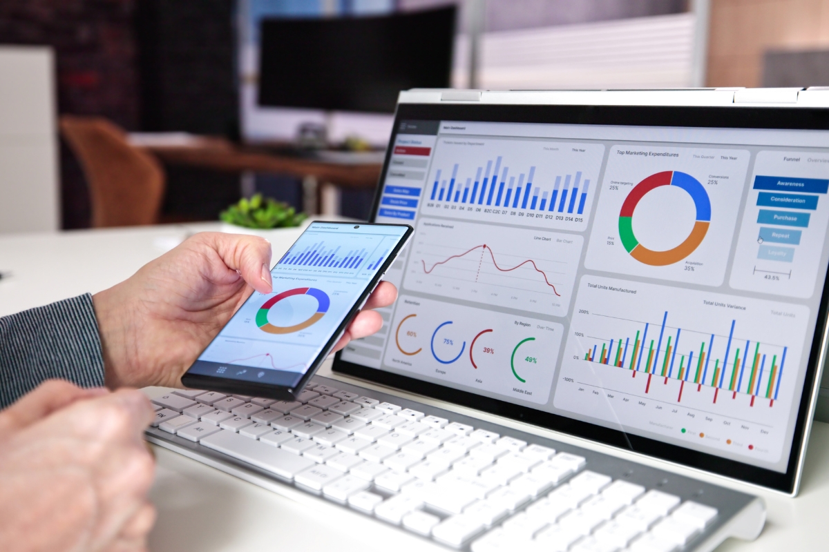Understanding User Behavior with Heatmaps: A Guide 6 A person reviews colorful business analytics charts, heatmaps, and graphs displayed on a laptop and smartphone at a desk with a keyboard.