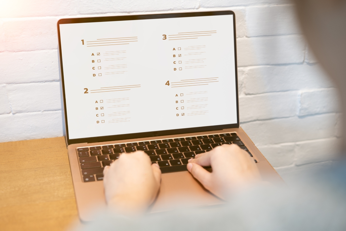 A person sits at a desk using a laptop displaying a multiple-choice quiz with four numbered questions on the screen, exploring must-have plugins to enhance their quiz experience.