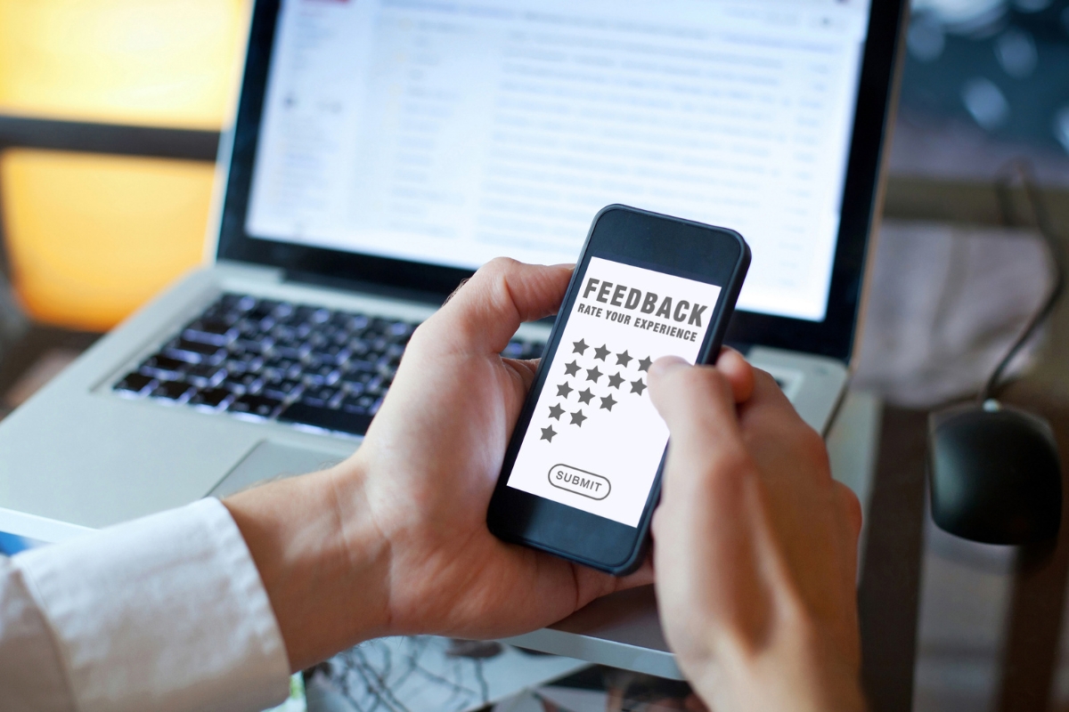 Optimizing for 'Near Me' Searches: A Guide for Local Businesses 5 Person holding a smartphone displaying a feedback form with star ratings, in front of an open laptop, highlighting the importance of reviews for 'near me' searches.