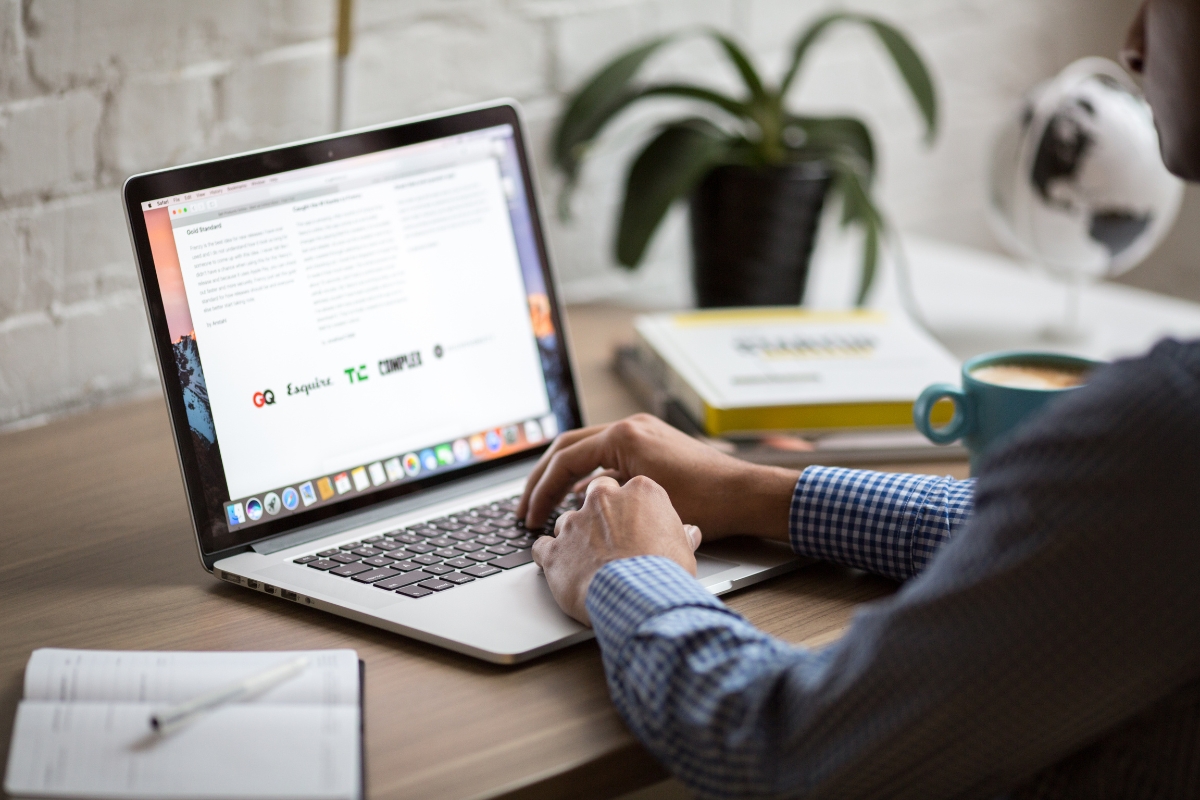 Optimizing for 'Near Me' Searches: A Guide for Local Businesses 6 A person types on a laptop at a wooden desk, researching 'near me' searches, with an open notebook, coffee mug, some books, and a potted plant nearby.