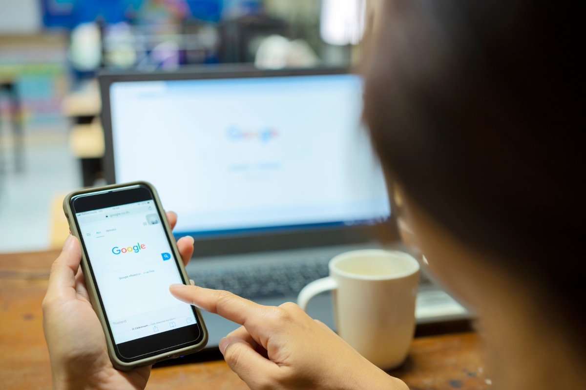 Optimizing for 'Near Me' Searches: A Guide for Local Businesses 3 A person uses Google Search on a smartphone to explore 'near me' searches, with a laptop displaying the Google homepage and a white mug in the background.