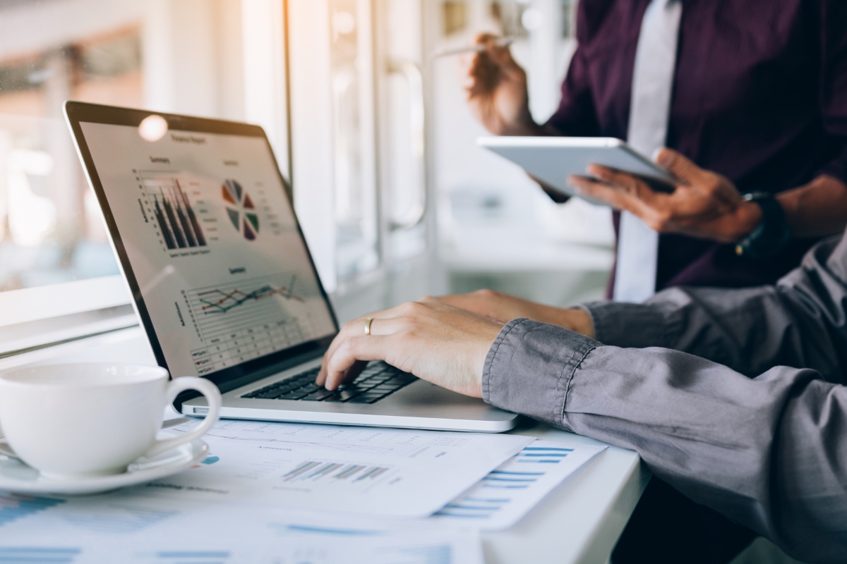 Storytelling in Marketing: Crafting Narratives that Resonate 7 Two people review business charts and graphs on a laptop and tablet at a desk, illustrating the power of storytelling in marketing with documents and a coffee cup nearby.