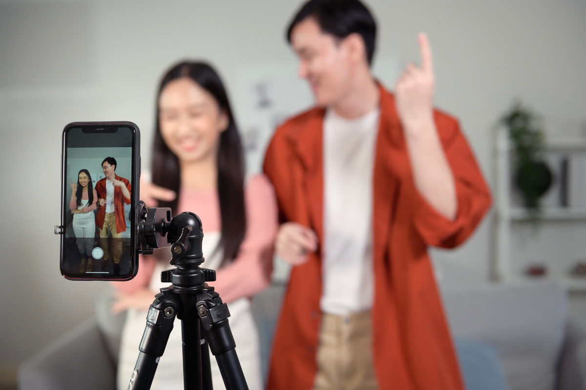 Harnessing the Power of TikTok for Business Marketing 3 Two people pose and smile in front of a smartphone mounted on a tripod, creating content indoors—perfect for showcasing Tiktok for business marketing strategies.