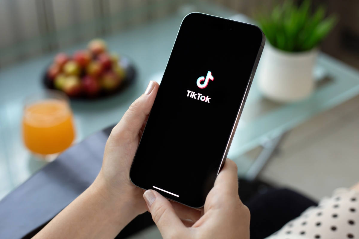 Harnessing the Power of TikTok for Business Marketing 4 A person holds a smartphone displaying the TikTok app logo, highlighting the potential of TikTok for business marketing, with a glass of orange juice and a bowl of fruit in the background.