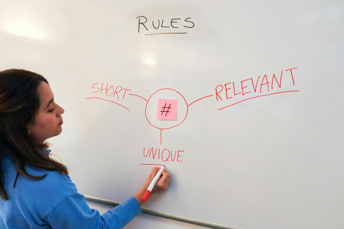Harnessing the Power of TikTok for Business Marketing 5 A person writes on a whiteboard, showing a diagram with a central hashtag symbol connected to "Short," "Relevant," and "Unique," under the heading "Rules"—illustrating key principles for Tiktok for business marketing.