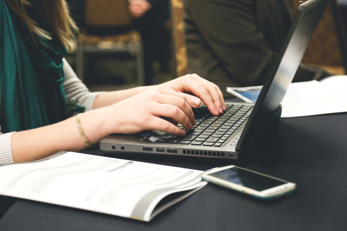 UX Conversion Rates Explained: How User Experience Drives More Sales 8 A person types on a laptop at a desk with a smartphone and an open document nearby, focusing on improving ux conversion rates for their latest project.