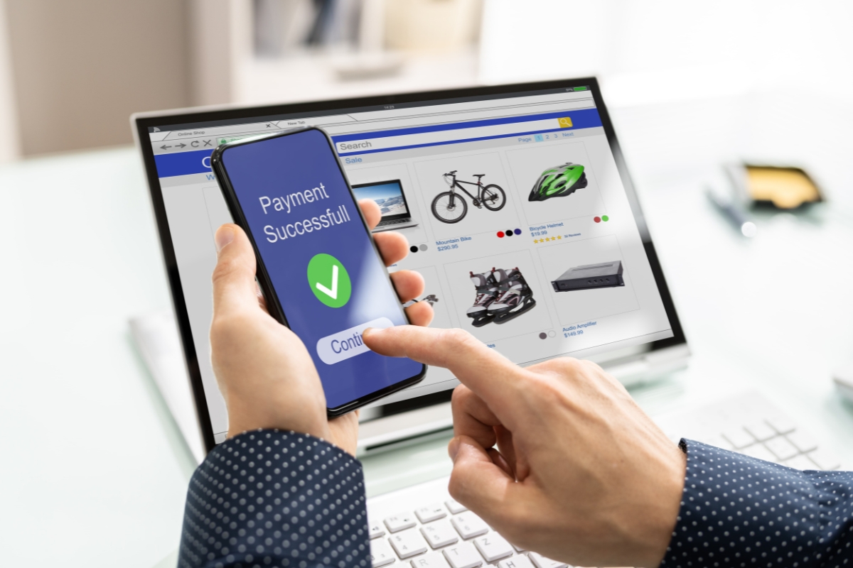 UX Conversion Rates Explained: How User Experience Drives More Sales 9 A person uses a smartphone for online shopping payment confirmation, enhancing ux conversion rates, with a laptop displaying sports equipment in the background.