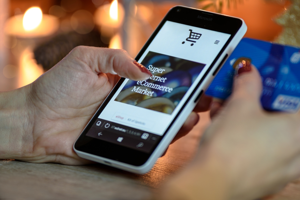 UX Conversion Rates Explained: How User Experience Drives More Sales 10 A person browses an online shopping website on a smartphone while holding a blue credit card in the other hand, showcasing how strong UX can boost conversion rates.
