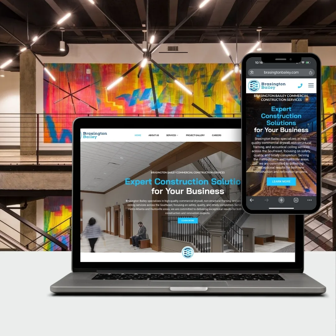 A laptop and smartphone display Brasington Bailey's construction company website, set on a table in front of a modern interior with colorful geometric wall art and metal railings.