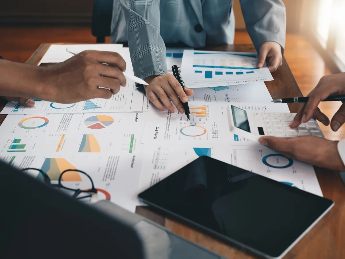Hands analyzing printed data reports with charts, graphs, and a calculator, illustrating the application of predictive analytics for marketing strategies.