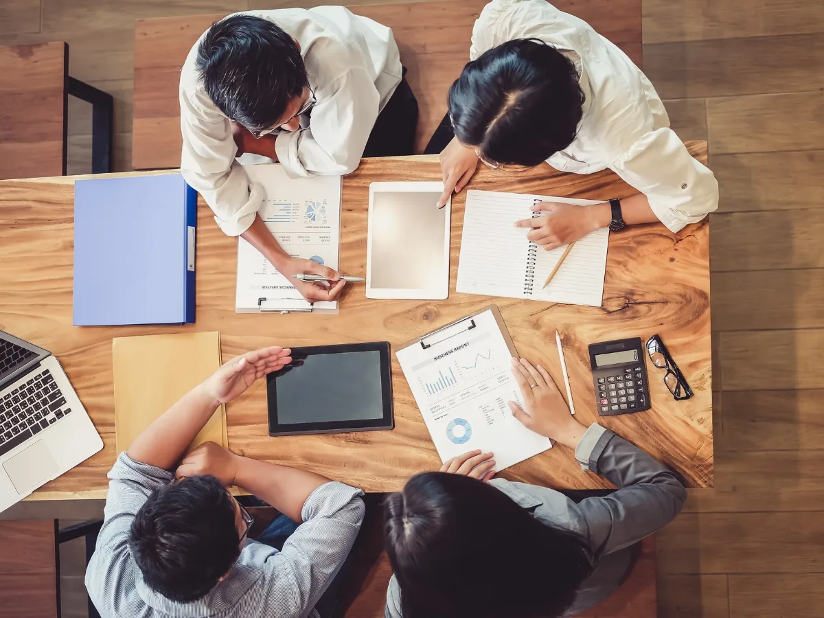 Group of professionals collaborating on predictive analytics strategies at a wooden table, with laptops, charts, and tablets, illustrating data-driven decision-making in marketing.
